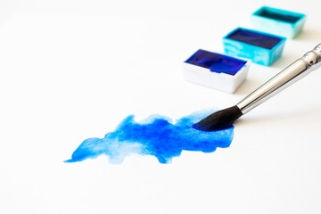 Close-up blue watercolor stain and paintbrush with selective focus on white paper. Home hobby and...