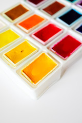 Close-up colorful watercolor palette box with selective focus on white background, top view. Concept creative and art
