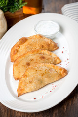 Three pasties on a white plate with sour cream