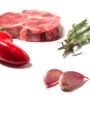 Garlic cloves in focus, rib eye steak,rosemary leafs and red chilli pepper out of focus. White isolated background.