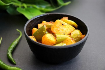 Indian food - Spicy Capsicum and potato stir fried with Indian spices. Aloo and Shimla Mirchi. served in the black plate over white background. 