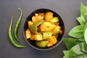 Indian food - Spicy Capsicum and potato stir fried with Indian spices. Aloo and Shimla Mirchi. served in the black plate over white background. 