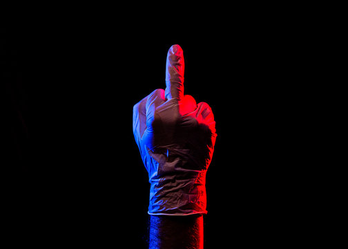 Latex-Handschuh zeigt Mittelfinger vor schwarzem Hintergrund bei Blaulicht und Rotlicht