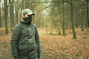 A man with a covered face looking around in an autumn forest