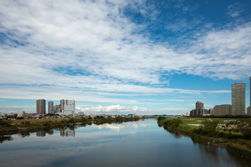 多摩川の川面を挟んで向かい合う川崎武蔵小杉ビル群と東京大田区側。多摩川に架かるガス橋から上流側を見た風景。
