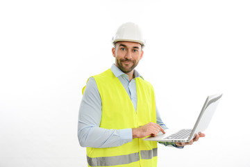 portrait of handsome foreman architect wearing yellow reflective vest and a hard hat using laptop...