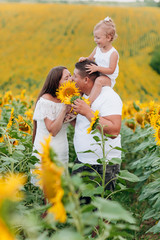 Daddy's carrying a baby daughter on his shoulders in the field of sunflowers. The concept of summer...