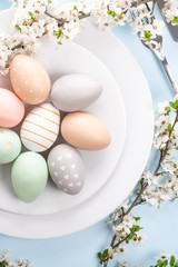 Easter table setting, holiday table home decor idea, flat lay composition with white plates, cutlery, colorful pastel painted Easter eggs, festive decor and fresh spring flowers