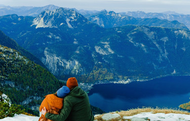 Fototapeta na wymiar Lovely family couple sitting on moutain peak with beautiful background and looking to landscape. Wonderful picture with copy space. Five fingers view point near Hallstatt village in Austria. Valley.