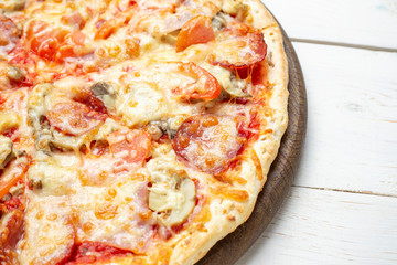 Pizza Francesca with cheese, champignon mushrooms, tomatoes and sliced meat on a white wooden background.
