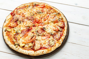Pizza Francesca with cheese, champignon mushrooms, tomatoes and sliced meat on a white wooden background.