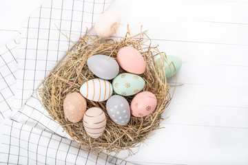 Easter table setting, holiday table home decor idea, flat lay composition with white plates, cutlery, colorful pastel painted Easter eggs, festive decor and fresh spring flowers