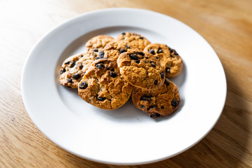 Choc chip cookies in a white plate on a wooden table. Close-up of homemade chocolate chip cookies. Basic drop cookies with chocolate morsels. Traditional handmade chewy cookies with chocolate chunk