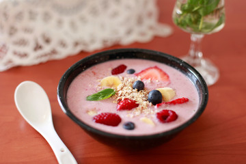 Bol de saludable smoothie de fresas con fruta fresca y avena en primer plano, con cuchara de cerámica, con fondo desenfocado