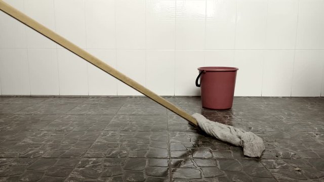 The girl washes the floors in the room with a rag on a mop.