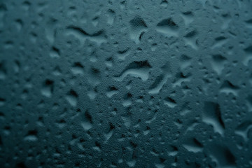 Texture of small and large drops on dark glass from rain on a green background