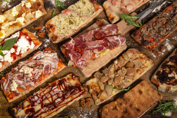 Assortment of rectangular homemade rustic pizza slices on wooden table.