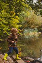 Fishing. Kid learning how to fish, holding a rod on a lake. Cute boy in hat fishing in a forest lake.