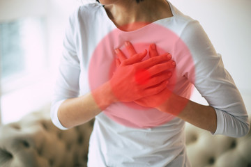Heart attack. Close-up photo of woman's hands touching her heart area highlighted in red, while she...