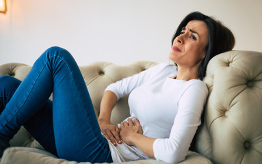 Abdominal pain. Young brunette woman is lying on a couch and crying while holding her stomach.