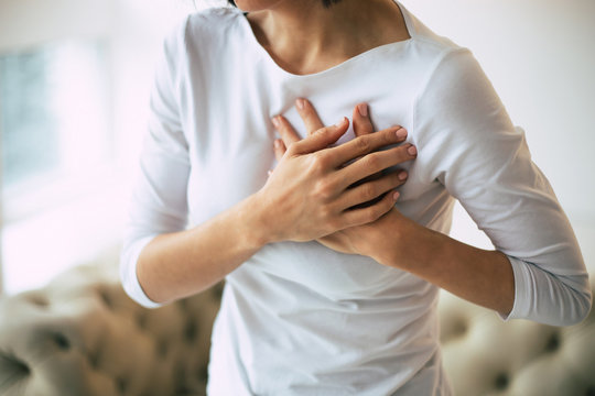 Heartache. Close-up Photo Of Woman's Hands Lying On Her Chest Because Of Her Severe Chest Pain.