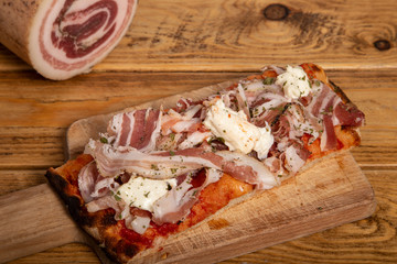 rectangular homemade slice of pork belly pizza on wooden table. Italian food