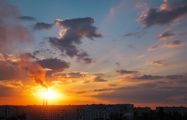 Colorful Magic Sunset. Roofs of city houses during sunrise. Birds flying in the sky. Dark smoke coming from the thermal power plant pipe.