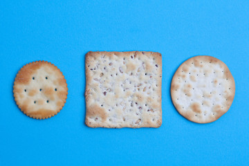Round and square salted crackers on blue background - top view with copy space