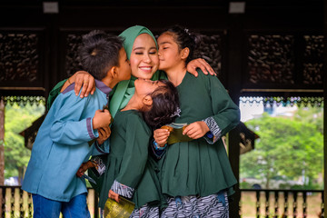 Happy children with an envelope of pocket money or raya angpao are kissing their mother during raya celebration. Malaysian Family and Raya Concept.