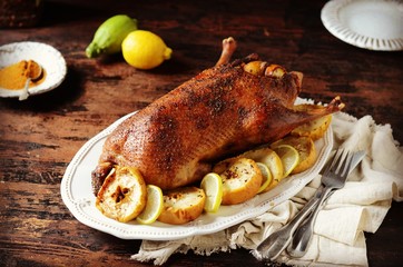 Traditional baked duck with apples and lemon on a dark wooden table, rustic style