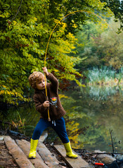 Naklejka na ściany i meble Little boy fisherman fishing in a lake with a fishing rod. Excited kid fishing on weekend.