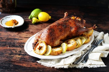 Traditional baked duck with apples and lemon on a dark wooden table, rustic style