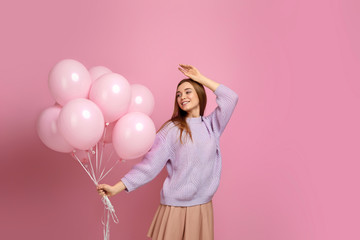 Smiling carefree girl in knitted sweater dancing with pastel pink air balloons isolated on pink background. Beautiful happy young woman on a birthday holiday. space for text