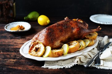 Traditional baked duck with apples and lemon on a dark wooden table, rustic style