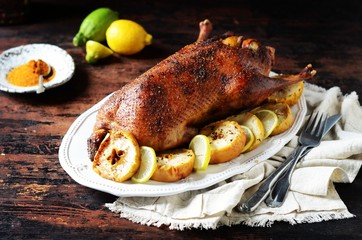 Traditional baked duck with apples and lemon on a dark wooden table, rustic style