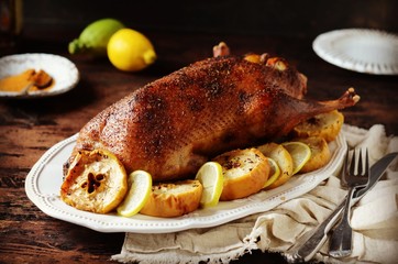 Traditional baked duck with apples and lemon on a dark wooden table, rustic style