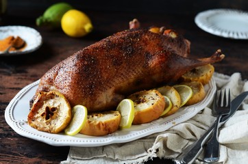 Traditional baked duck with apples and lemon on a dark wooden table, rustic style