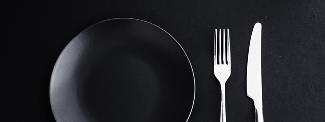 Empty plates and silverware on black background, premium tableware for holiday dinner, minimalistic...