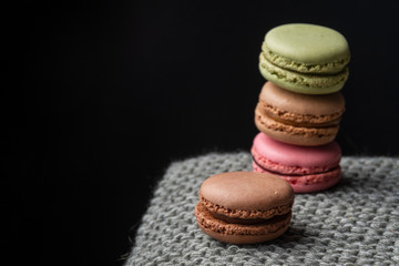 Close-up of stacked macarons, with selective focus, on gray knitted blanket and black background, horizontally, with copy space