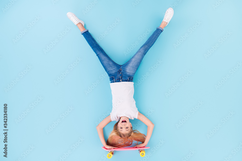 Wall mural Top above high angle view full body photo of positive girl sporty kid ride longboard upside down show tongue out wear white clothes lay isolated over blue color background