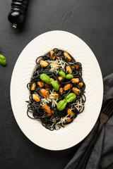 Black pasta spaghetti squid Ink with mussels in white plate on black. Top view. Vertical format.