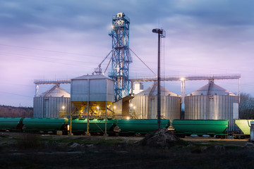 Modern steel agricultural grain granary silos cereal storage warehouse loading railway cargo carriage at night or sunrise. Agribuisness farmland rural industry landscape scene. Mill store facility © Kirill Gorlov