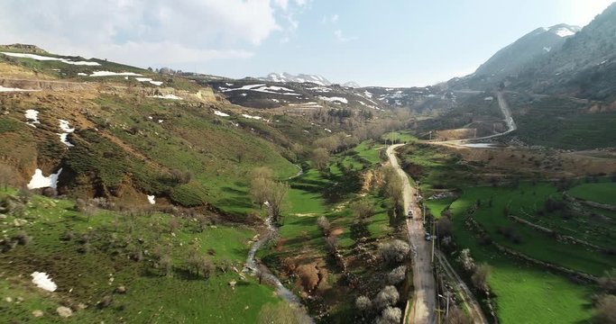 Aerial backward shot of car traveling on country road in scenic landscape