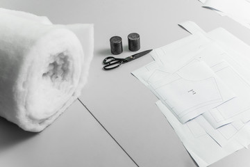 Work Desk of a clothing designer in an Atelier or textile factory. A large roll of synthetic lining fabric, tailor's scissors, kettlebells and paper patterns - the tailor's workflow tools top view