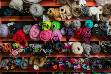 Shelves with laid out rolls of multicolored fabric for sale in a fabric store or at a garment textile factory. Colorful background.