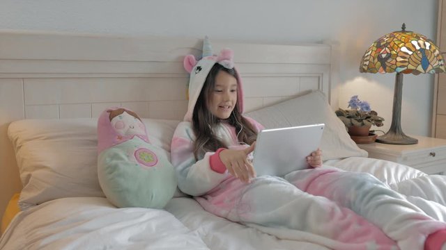 joven tumbada en la cama  y con pijama unicornio de capicha llama feliz por video grupal con tableta
