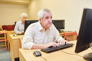 Senior Mann sitzt am PC in einem Computerkurs der VHS oder im Seniorenheim