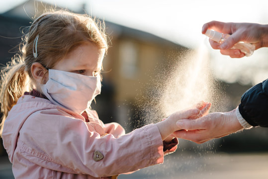 Coronavirus. Woman use spray sanitizer on hands child  in a protective mask on the street. Preventive measures against Covid-19 infection. Аntibacterial hand-washing spray. Illness protection.