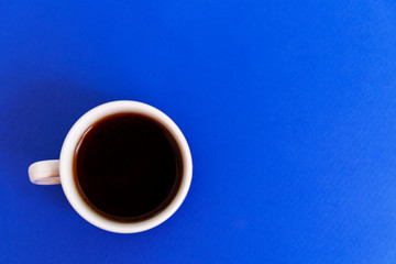White cup with strong black coffee on a blue background. Top view. Space for text.