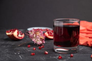 Glass of pomegranate juice on a black concrete background. Side view, copy space.